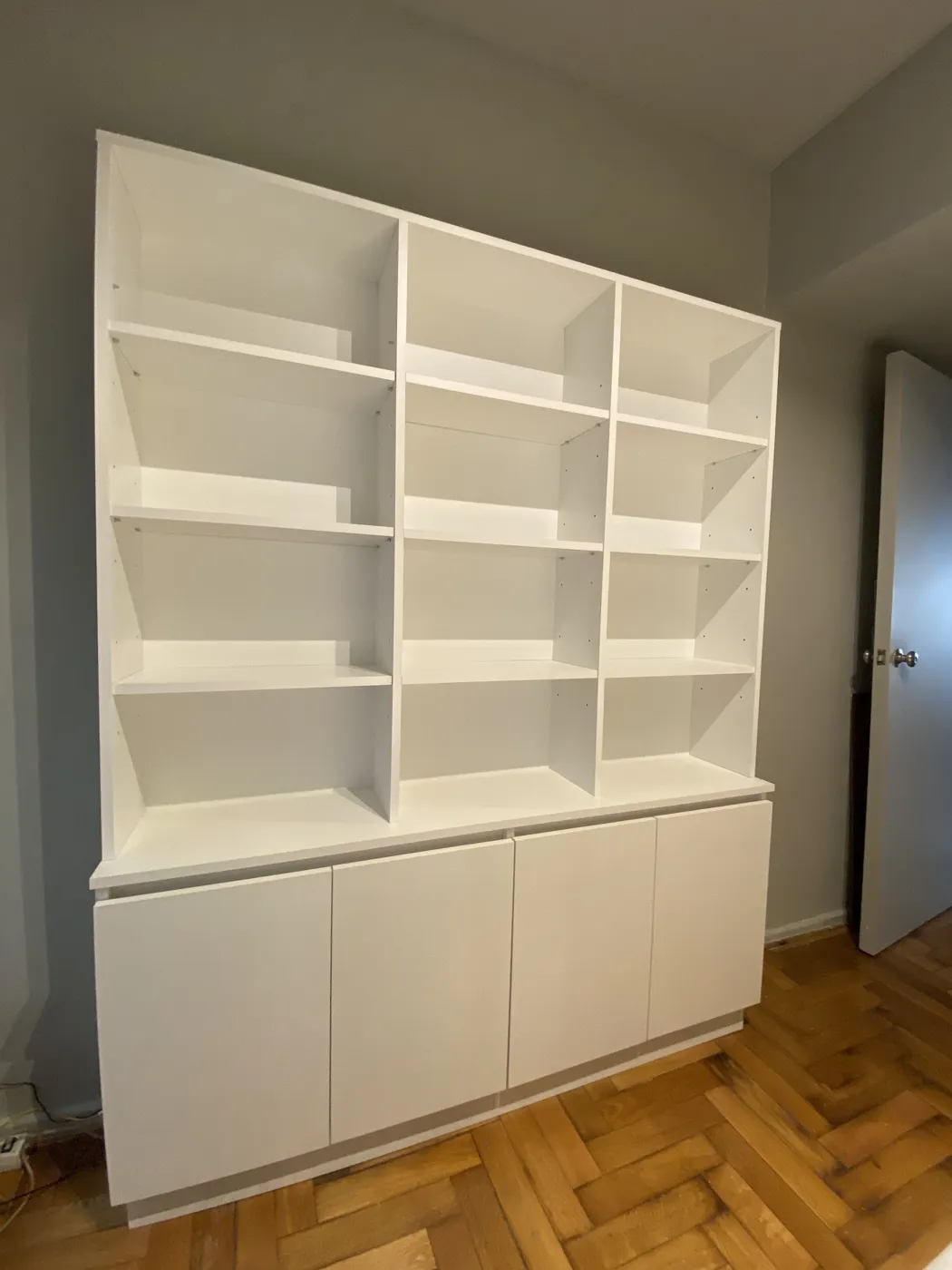 Biblioteca blanca a medida con estantes abiertos y bajo mueble con puertas, sobre piso de parquet