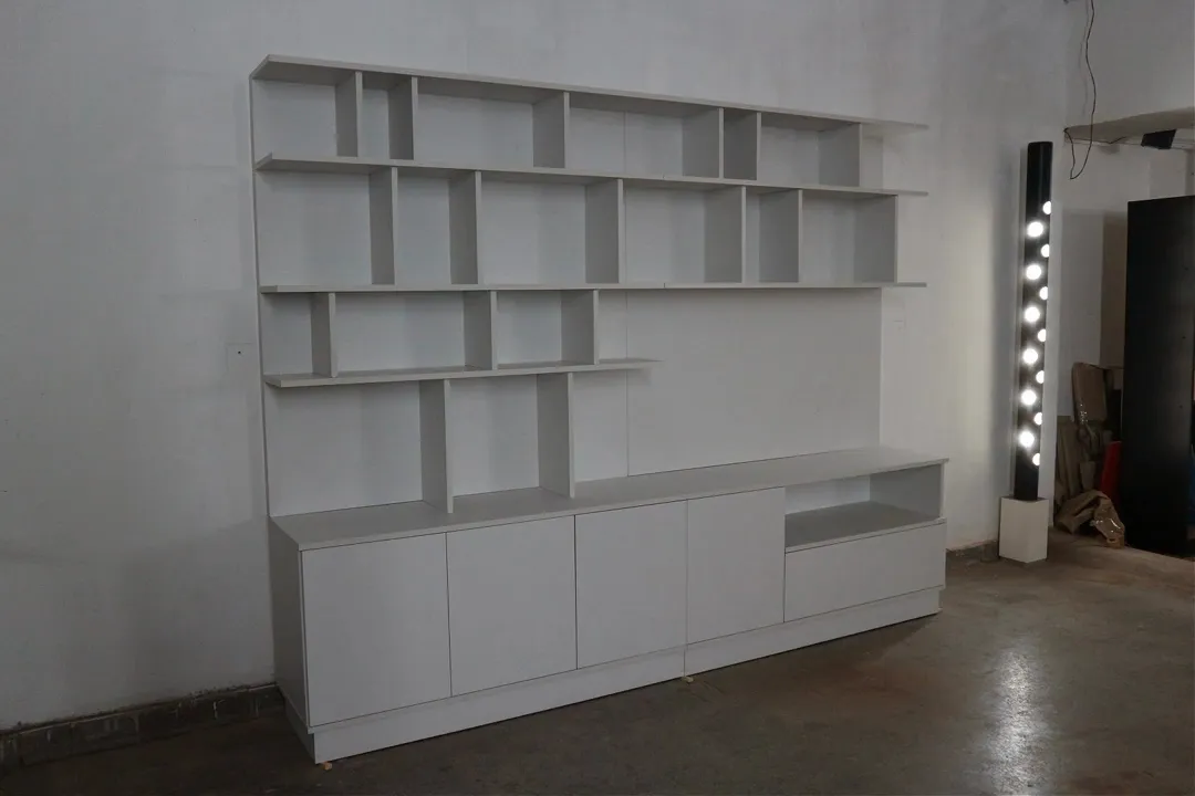 Biblioteca blanca de pared completa con estantes abiertos de distintos tamaños y cajones abajo