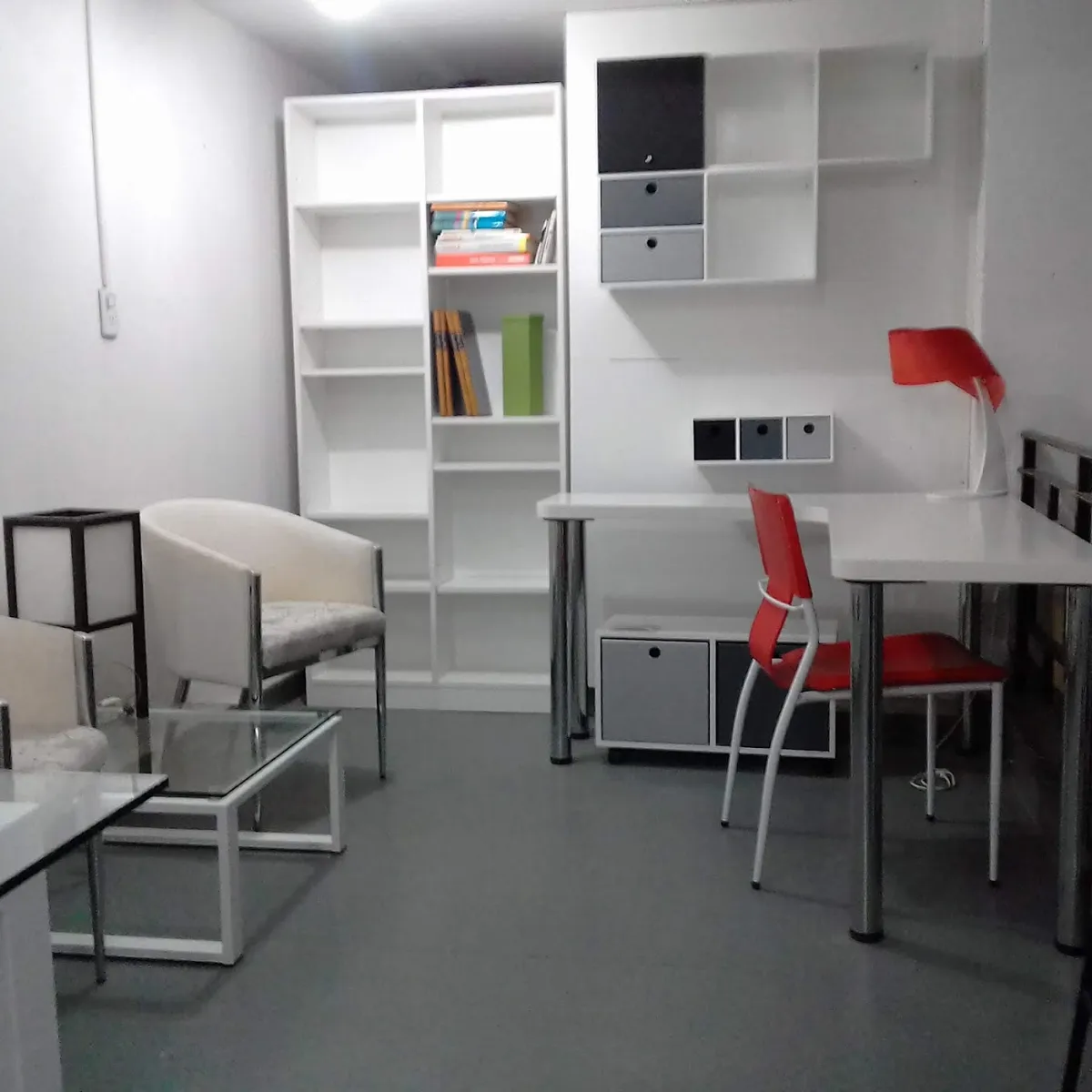 Escritorio blanco con biblioteca y cajas grises en un cuarto chico