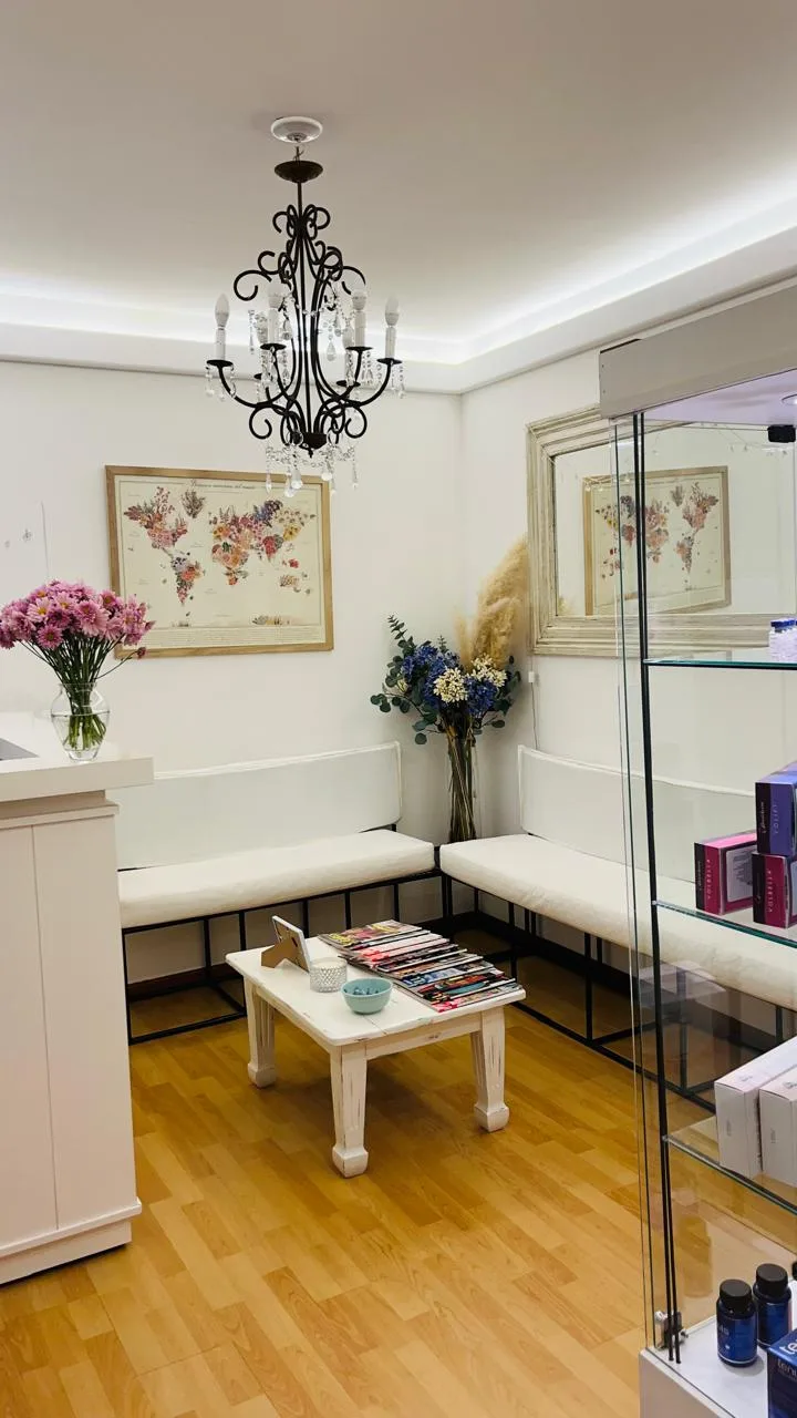 Sala de espera luminosa con araña, sillones blancos, flores y cuadros