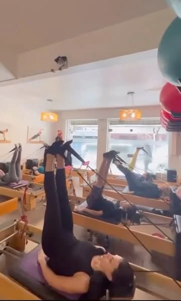 Alumnas acostadas en el reformer con las piernas en alto sostenidas por las cintas