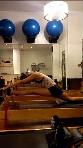 Alumna estirando en el reformer con una pierna extendida sobre la barra