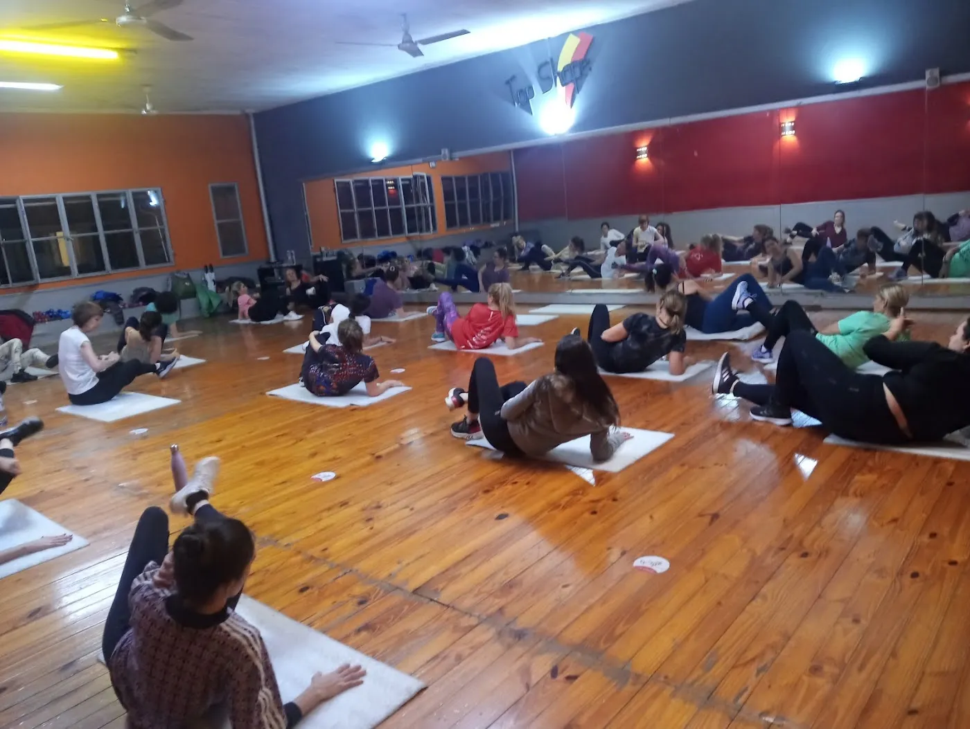 Clase grupal sobre colchonetas en el salón de piso de madera con paredes naranja, roja y azul